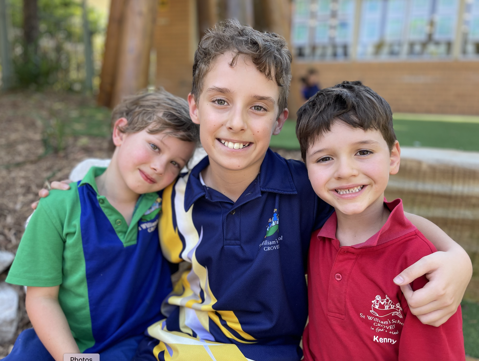 Three students in school uniform standing together outdoors with their arms around each other.