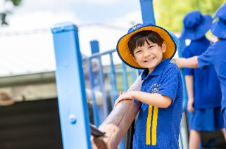 Student in school uniform playing on playground equipment outdoors.