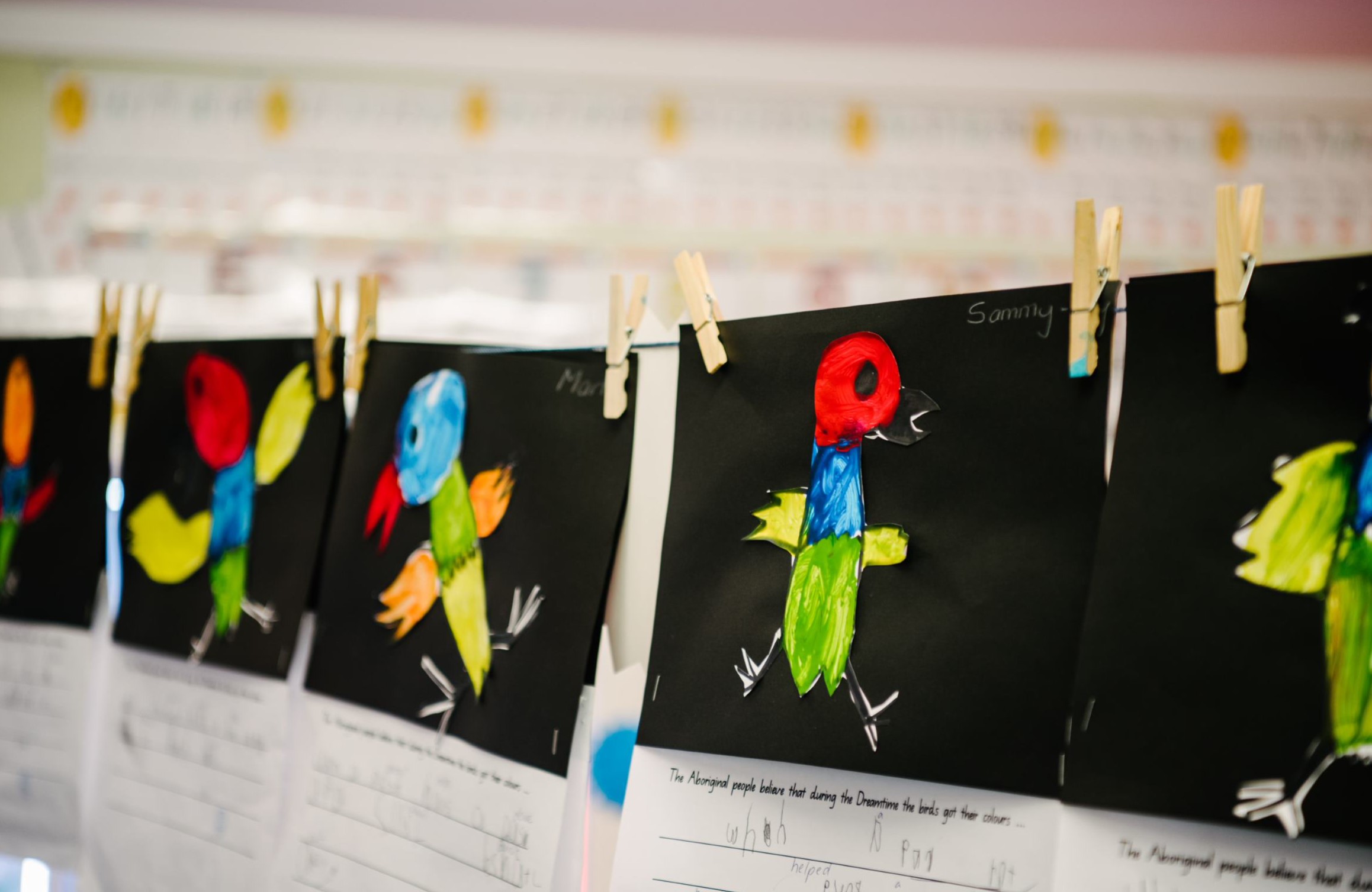 Student artwork of colourful birds displayed on a line in a classroom.
