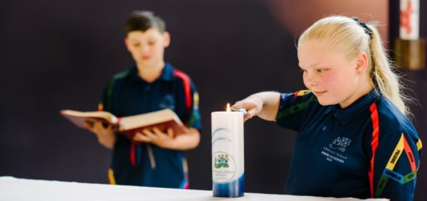 Students participating in a school prayer activity with a candle and reading.