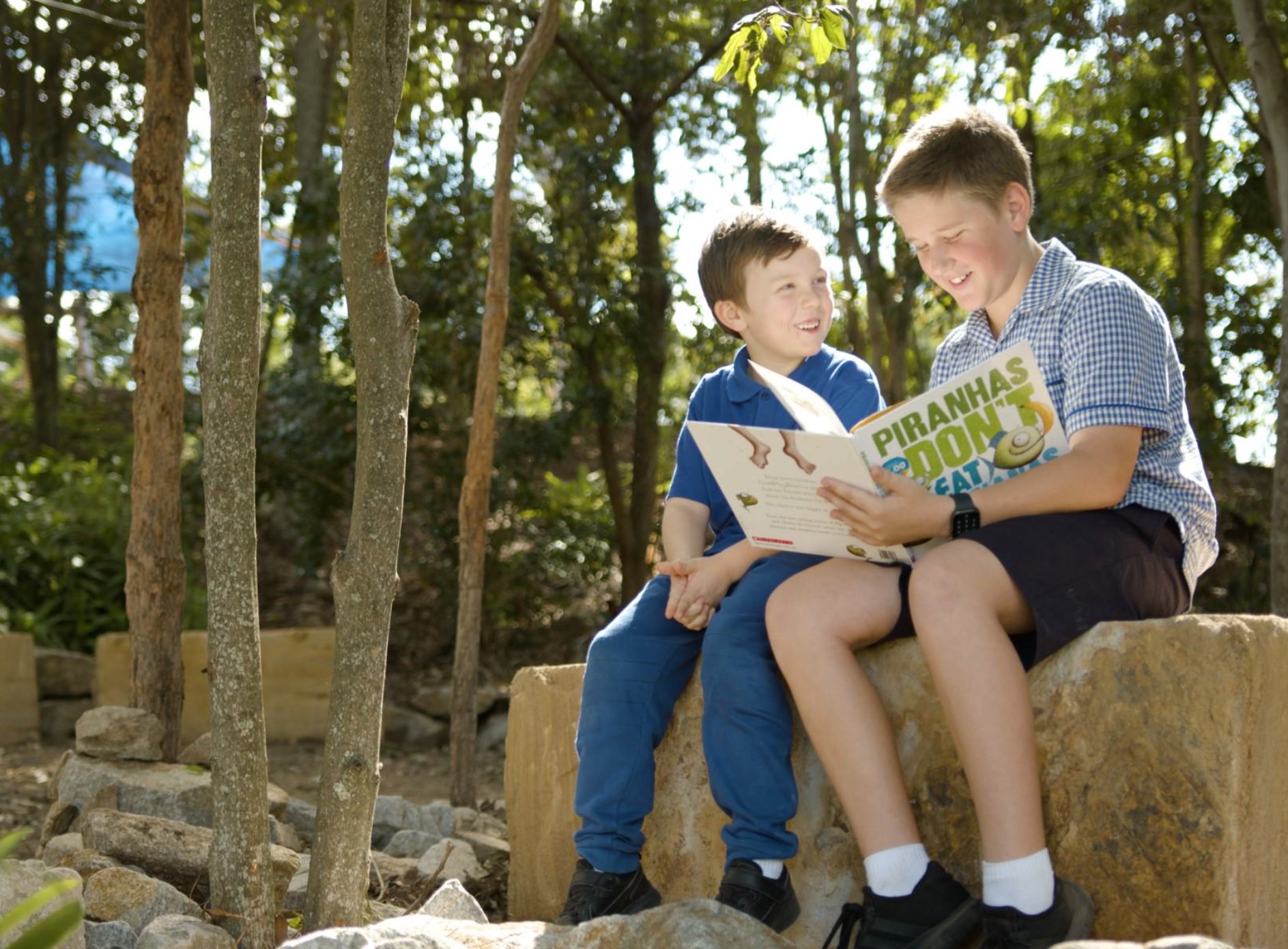 Two students sitting outdoors reading a book together on a stone seat.