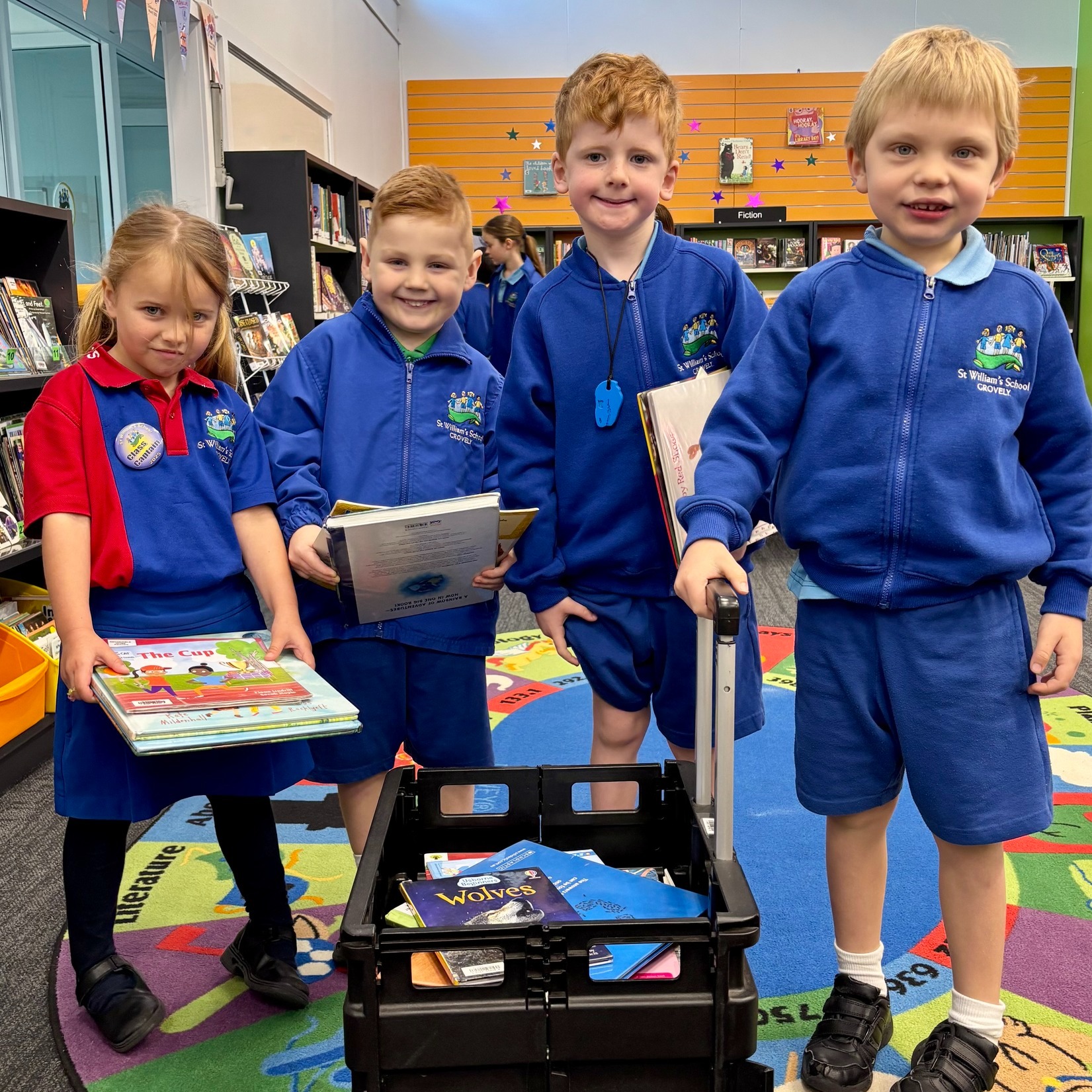 Students in school uniform holding library books beside a book trolley.