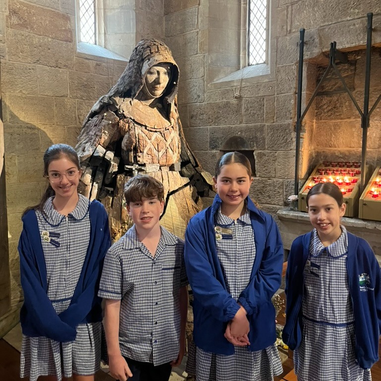 Students in school uniform standing inside a church near a religious statue.