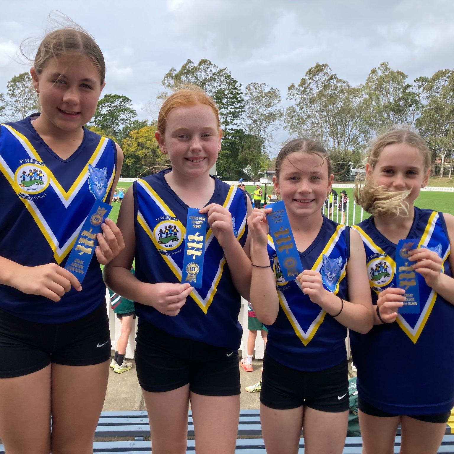 Students in school sports uniforms holding participation ribbons at a school sporting event.
